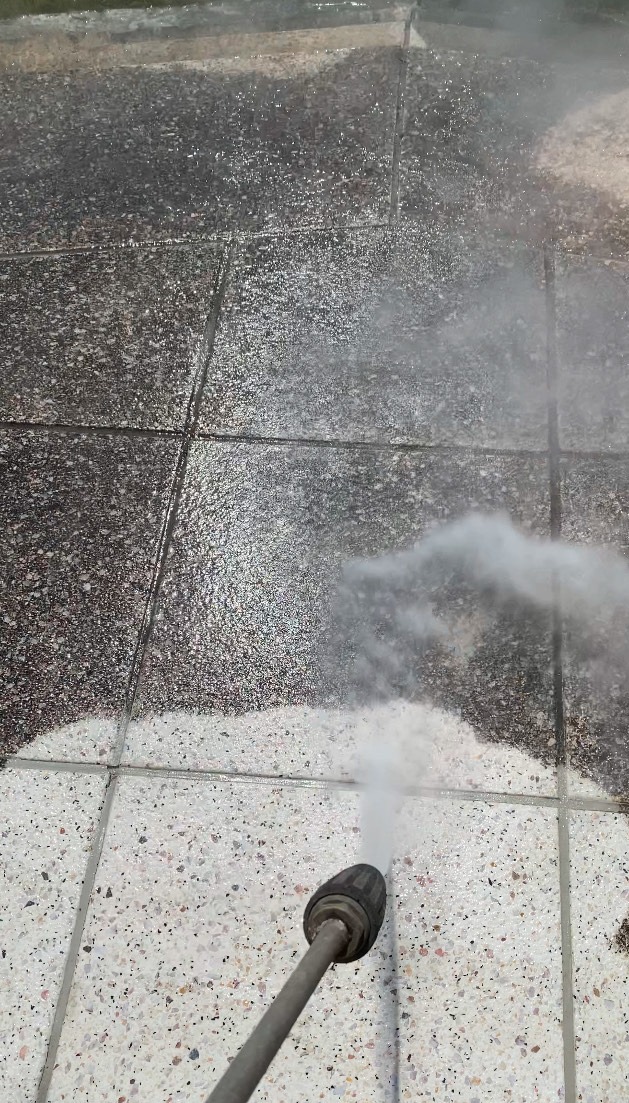 Dysza myjki ciśnieniowej czyści kostkę brukową. Widoczna różnica między czystą, a brudną powierzchnią. Strumień wody pod ciśnieniem usuwa zabrudzenia.