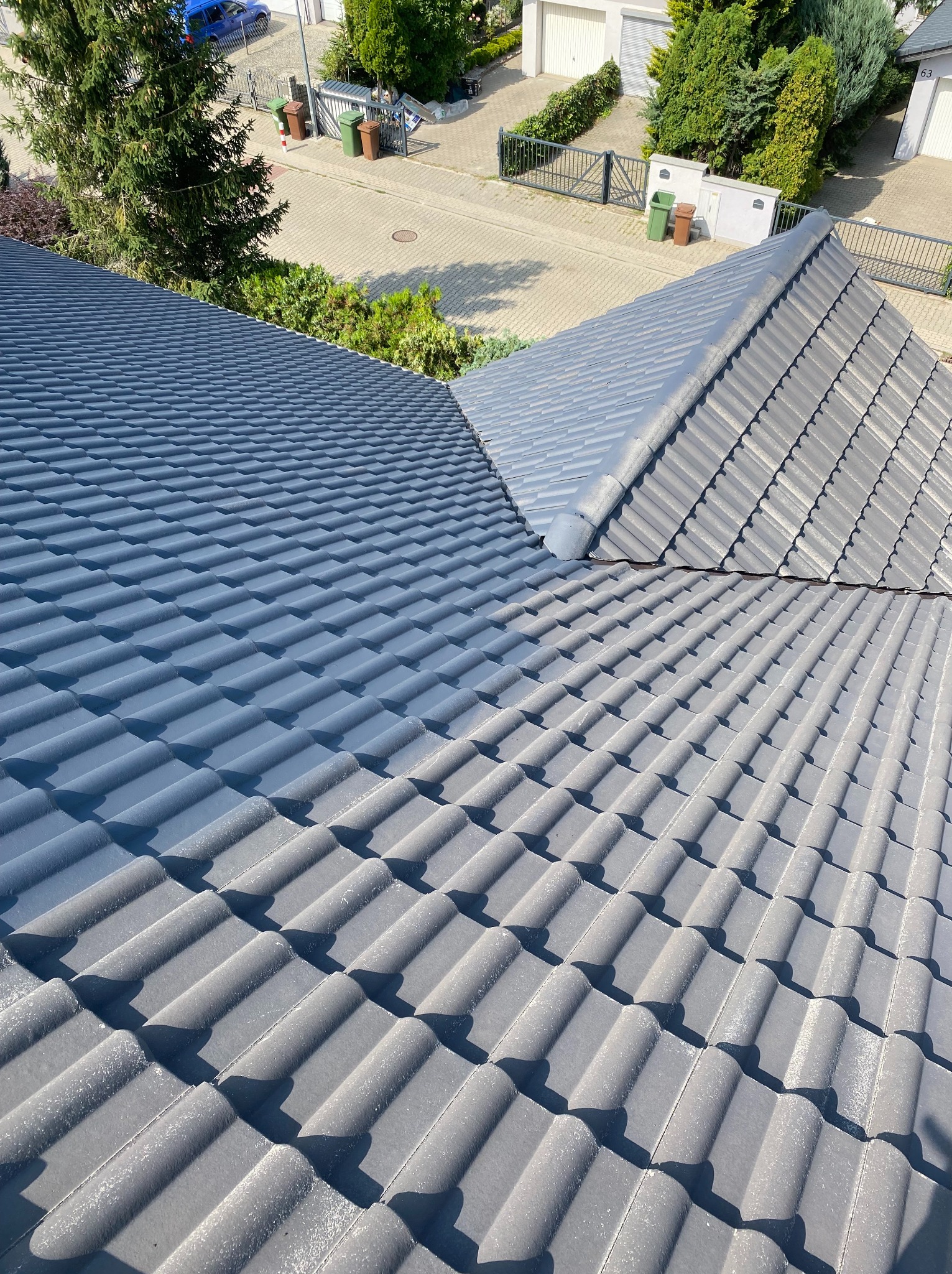 Częściowo umyty, szary dach z dachówki ceramicznej, widok z góry. W tle zabudowa jednorodzinna i zieleń. Widoczna różnica w kolorze dachówek.