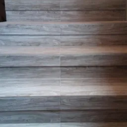 Schody wyłożone płytkami imitującymi drewno w odcieniach szarości i brązu, widok z dołu na g&oacute;rę, fuga w kolorze szarym.