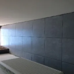 Szara ściana wykończona panelami imitującymi beton, z widocznym grzejnikiem i fragmentem drewnianej konstrukcji okiennej w tle.