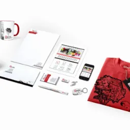 Zestaw artykułów promocyjnych firmy Mardo: koszulka z grafiką, kubek, torba papierowa, wizytówki, długopis, notes, tablet, telefon i inne gadżety z logo firmy, ułożone na białym tle.