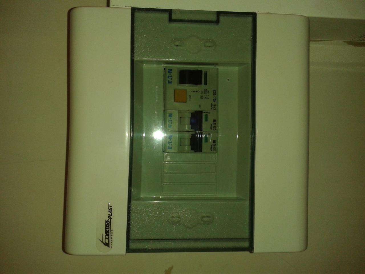 Zamknięta, biała skrzynka elektryczna firmy Elektro-Plast z widocznymi bezpiecznikami Eaton wewnątrz, zamontowana na ścianie, oświetlona z góry.