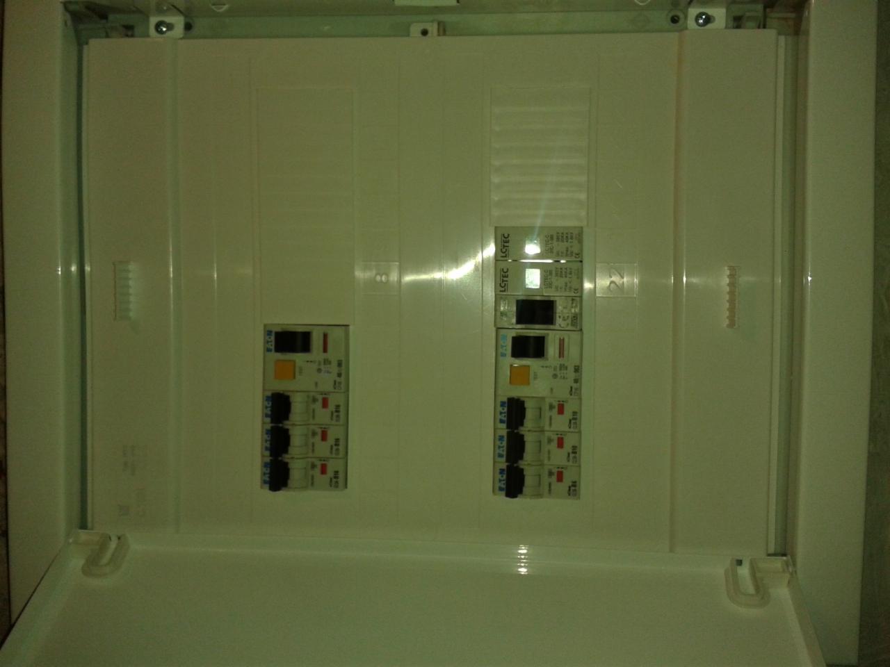 Otwarta skrzynka elektryczna z zamontowanymi bezpiecznikami Eaton i LSTEC, widoczne oznaczenia na urządzeniach.