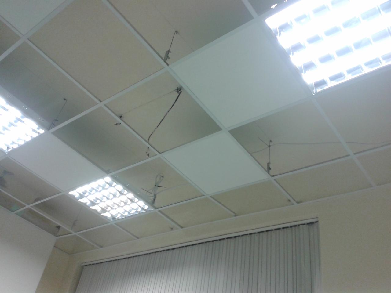 Sufit podwieszany z widocznymi kablami i oświetleniem rastrowym, widok z dołu, w tle żaluzje.