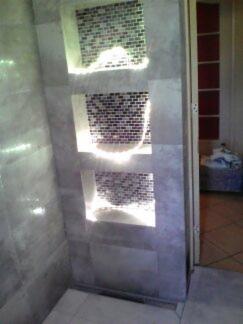 Ściana wyłożona marmurkowymi płytkami z trzema wnękami wykończonymi mozaiką, podświetlonymi od wewnątrz, widoczne niedoskonałości w ułożeniu płytek i słabe oświetlenie.