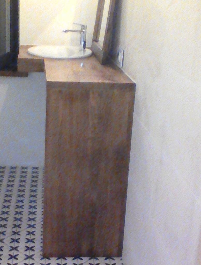 Umywalka nablatowa z chromowaną baterią na drewnianym blacie, wzorzyste płytki podłogowe.