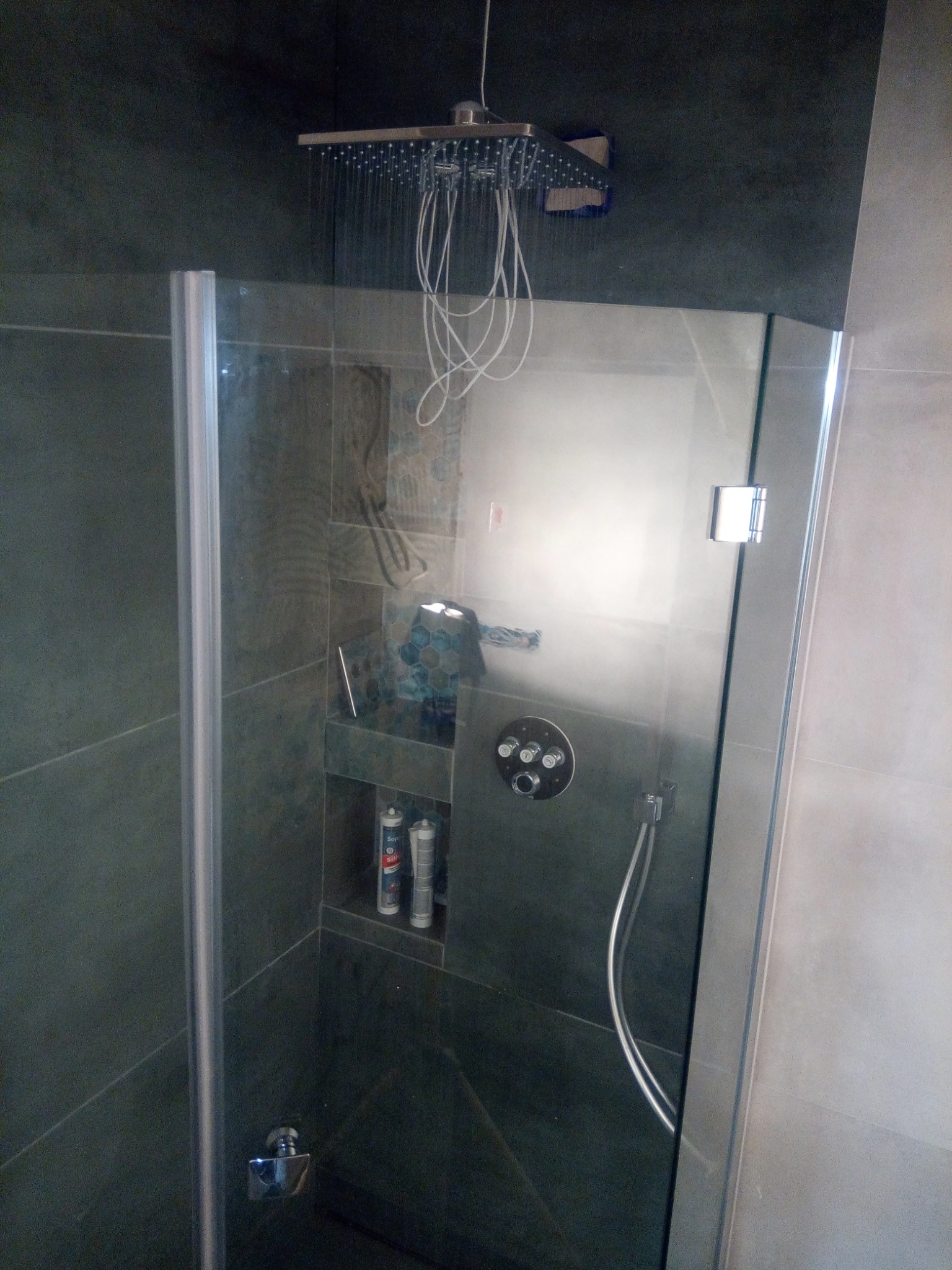 Nowoczesna kabina prysznicowa z deszczownicą, wnęką na kosmetyki i szarymi płytkami imitującymi kamień.