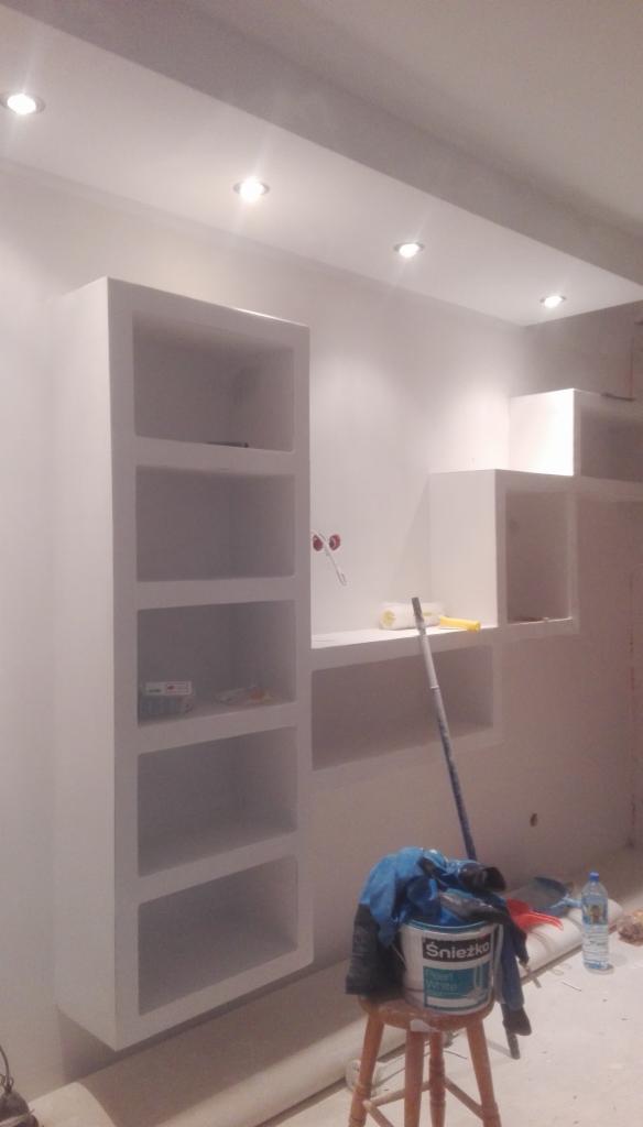 Białe, pomalowane na gładko ściany z wnękami w trakcie wykańczania, widoczny kubeł z farbą Śnieżka i narzędzia malarskie.