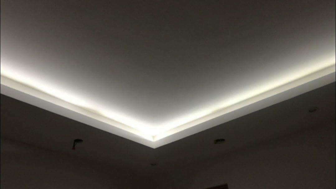 Podwieszany sufit z oświetleniem LED w narożniku pomieszczenia, widoczne otwory na oświetlenie punktowe.