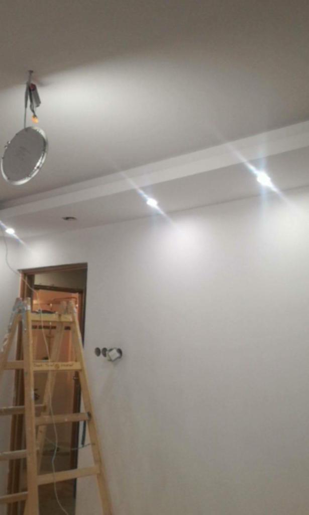 Wnętrze w trakcie wykańczania: widoczna drabina oparta o świeżo pomalowaną ścianę z zainstalowanymi punktowymi lampami sufitowymi; wisząca lampa tymczasowa.
