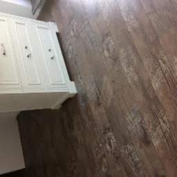 Ukończona podłoga z paneli o wzorze imitującym stare drewno z nadrukami w stylu vintage, widoczna szafka w tle.