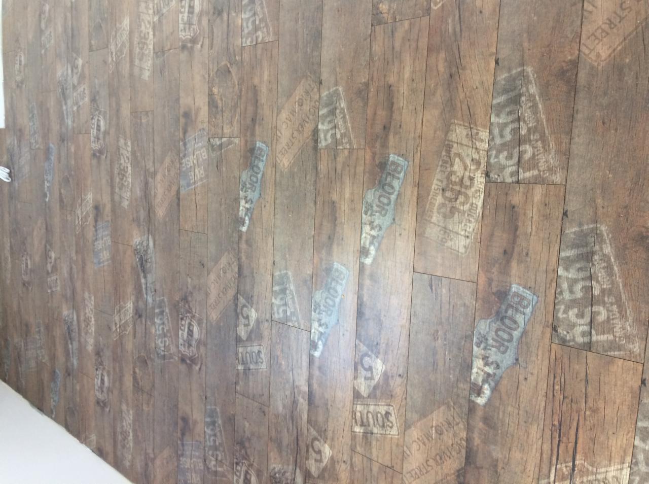 Ułożona podłoga z paneli laminowanych imitujących drewno z nadrukowanymi motywami starych tablic rejestracyjnych i nazw ulic, sfotografowana pod kątem.