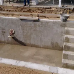 Wykop pod taras z betonowymi schodami w trakcie budowy, widoczne przygotowane podłoże, instalacja wodna i fragment układanej kostki brukowej wokół.