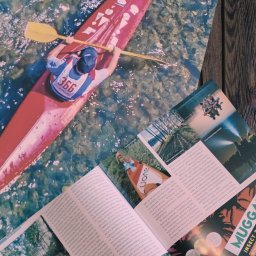 JW Projekt - Okładka magazynu kajakowego 'Wiosło' z kajakarzem na wodzie i otwarte strony z artykułami o spływach kajakowych, leżące na drewnianym stole.