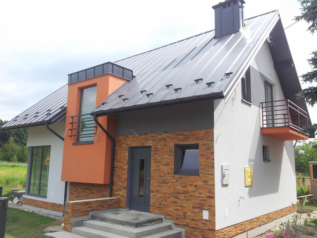 Nowoczesny dom jednorodzinny z elementami elewacji z cegły klinkierowej i metalową blachodachówką w kolorze grafitowym.