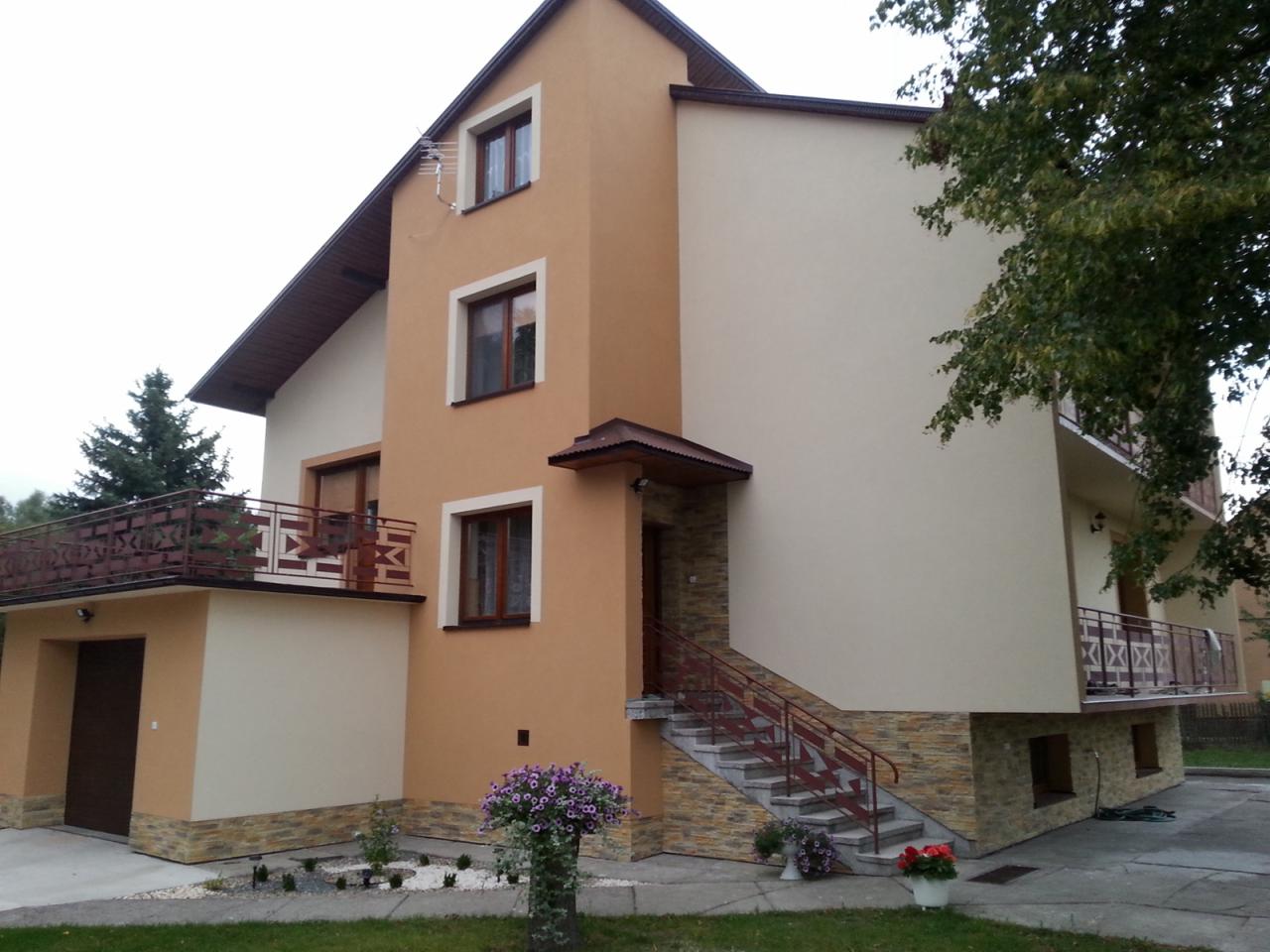 Dwukondygnacyjny dom z elewacją w odcieniach beżu i brązu, z balkonami o metalowych balustradach i schodami wejściowymi wykończonymi kamieniem dekoracyjnym.