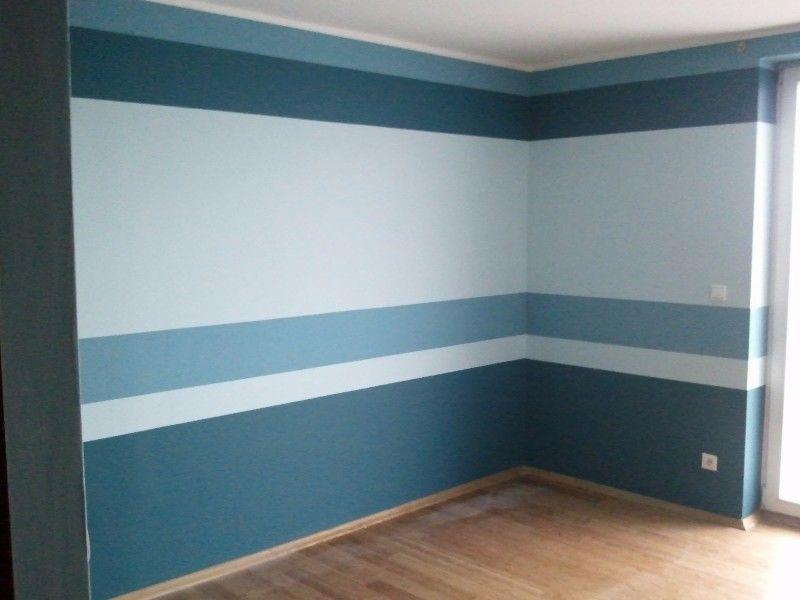 Pomieszczenie po malowaniu ścian w poziome pasy w odcieniach błękitu i szarości, z drewnianą podłogą i białymi kontaktami na ścianach.