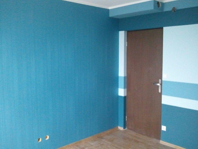 Pomieszczenie po malowaniu ścian na turkusowo i błękitno z brązowymi drzwiami i widocznymi dwoma otworami w ścianie.