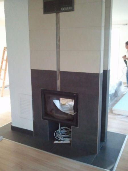 W trakcie montażu dwukolorowego kominka z czarnym wkładem, widoczne kable i fragment drabiny w tle.