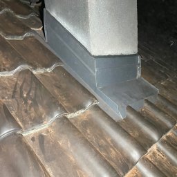 ART-DACH Dawid Mikołajczak - Szare, metalowe wykończenie komina na brązowym dachu z dachówki ceramicznej, widoczne elementy wentylacyjne.