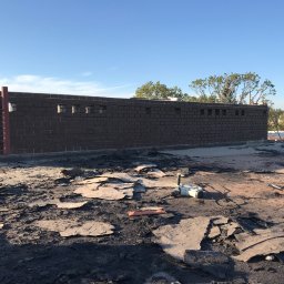 ART-DACH Dawid Mikołajczak - Demontaż starego pokrycia dachowego na płaskim dachu, widoczny fragment muru attyki z cegły klinkierowej i narzędzia pracy. Lokalizacja Wrocław Zakopiańska.