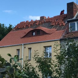 ART-DACH Dawid Mikołajczak - Częściowo zdjęty dach z czerwonej dachówki na żółtym budynku mieszkalnym we Wrocławiu, dekarz w czerwonej koszulce układa nową dachówkę.