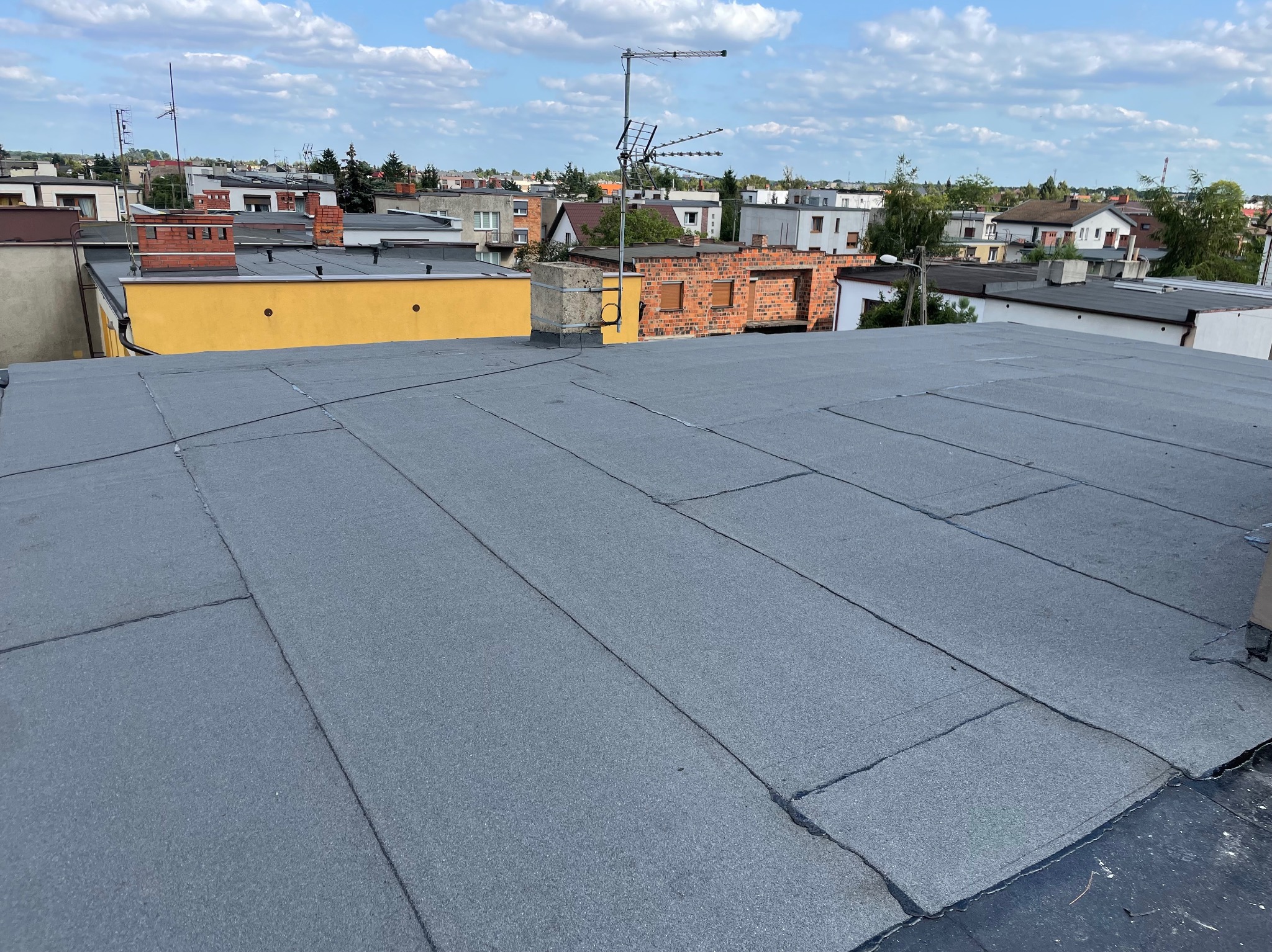 Nowe, płaskie pokrycie dachowe z papy termozgrzewalnej na budynku we Wrześni, widok z góry na tle zabudowy miejskiej i pochmurnego nieba.