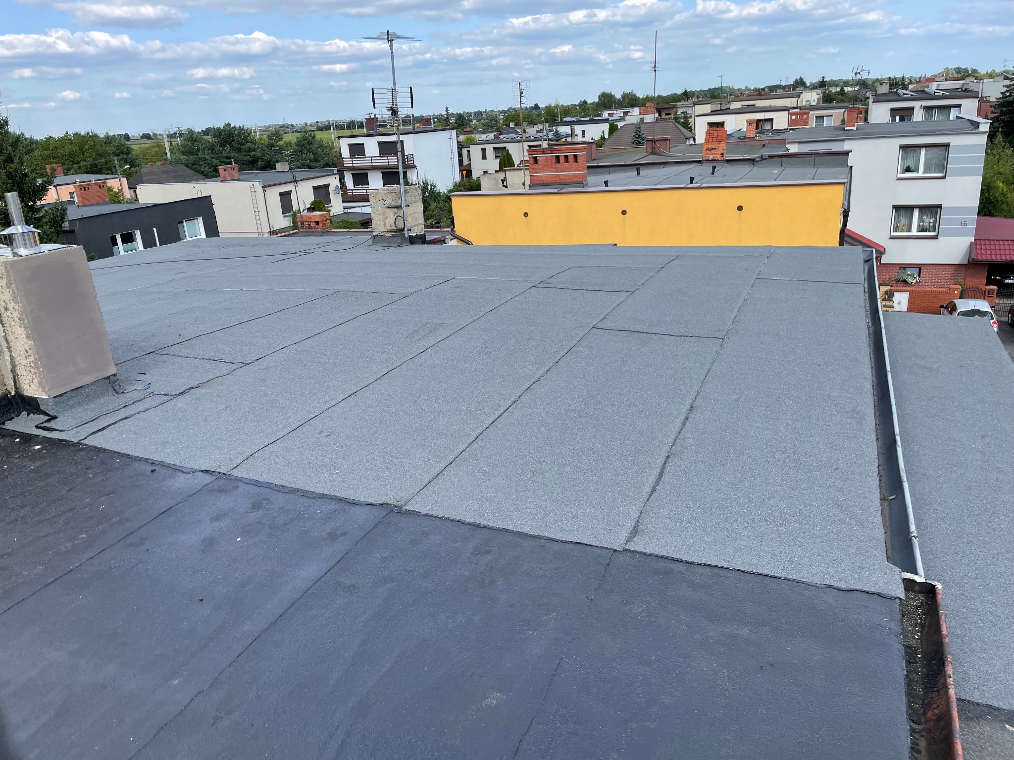 Wykończony dach płaski pokryty papą termozgrzewalną na tle zabudowy mieszkalnej we Wrześni.