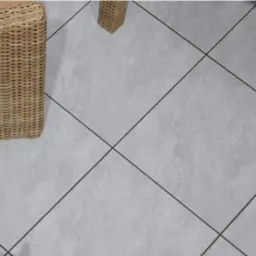 Szare płytki tarasowe ułożone diagonalnie z ciemnymi fugami, fragmenty mebli z rattanu i rośliny w lewym dolnym rogu.