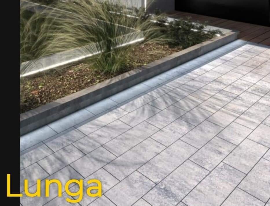 Szara nawierzchnia z prostokątnych płyt ułożonych w regularny wzór, obok podwyższona rabata z roślinami i oświetleniem LED