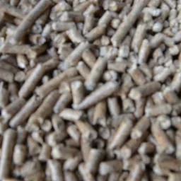 Stos brązowawych granulek biomasy, prawdopodobnie paliwa opałowego, z widocznymi śladami obróbki, sfotografowany z bliska, z niewielką głębią ostrości.