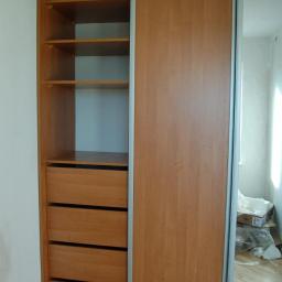 Meble kuchenne z drewna Grzegorz Jeziorski - Jasna, drewnopodobna szafa przesuwna z lustrem i otwartą częścią z półkami i szufladami, widoczna na tle pokoju w trakcie remontu.