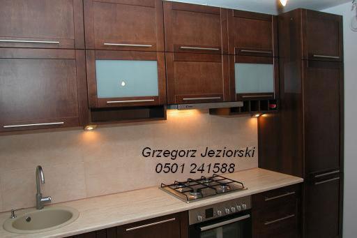 Ciemnobrązowa zabudowa kuchenna z matowymi, szklanymi frontami szafek wiszących, oświetleniem punktowym pod szafkami i blatem w kolorze beżowym, zlokalizowana w Warszawie.