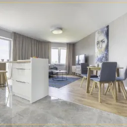 Nowoczesne wnętrze mieszkania z aneksem kuchennym, marmurową podłogą, stołem jadalnym z szarymi krzesłami i obrazem na ścianie.