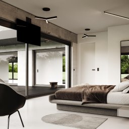 Design Studio Jacek Łuczak - Nowoczesna sypialnia z betonowymi elementami, dużym oknem przesuwnym i minimalistycznym oświetleniem. Widoczny fragment łóżka, krzesło i dywan.