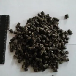 Kupa ciemnych, brązowych granulek obok czarnej miarki na białym papierze, ukazująca ich rozmiar.