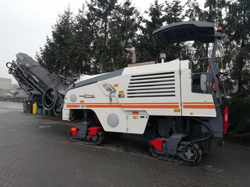 Frezarka do asfaltu Wirtgen W 190 F na gąsienicach, zaparkowana na brukowanym placu, z widocznymi elementami roboczymi i zbiornikiem na urobek.