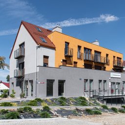 Eco Sense Sp. z o.o. - Nowoczesny budynek z elewacją w odcieniach szarości, bieli i żółci, balkony z czarnymi balustradami, czerwony dach i częściowo widoczne niebo.