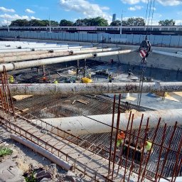 Eco Sense Sp. z o.o. - Budowa fundamentów z rurami ochronnymi i zbrojeniami; widoczni pracownicy i dźwig. Etap prac ziemnych i konstrukcyjnych w otoczeniu miejskim.