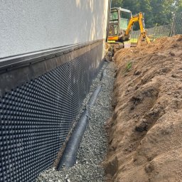 Geo-Bau Chmielarski - Ocieplenie fundamentów budynku z folią kubełkową, drenażem i warstwą żwiru. W tle koparka. Budowa fundamentów w trakcie realizacji.