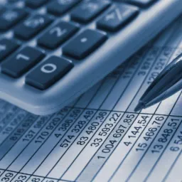 Kalkulator, długopis i arkusz kalkulacyjny z liczbami w odcieniach niebieskiego, z wyraźnie widoczną wartością 1 004 697.85.