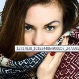 Portret kobiety z wyraźnym makijażem oczu, czerwonym lakierem na paznokciach i dużym wzorzystym szalikiem zasłaniającym część twarzy.