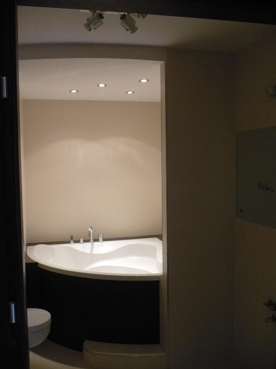 Nowoczesna, narożna wanna w łazience z ciemnymi panelami i punktowym oświetleniem sufitowym.