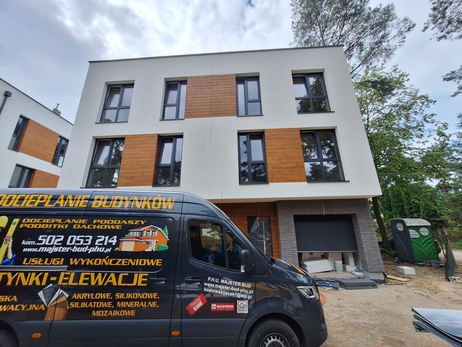 Nowoczesny dom z ocieploną elewacją, wykończony drewnianymi panelami. Na pierwszym planie firmowy bus z reklamą usług ocieplania i wykończeń.