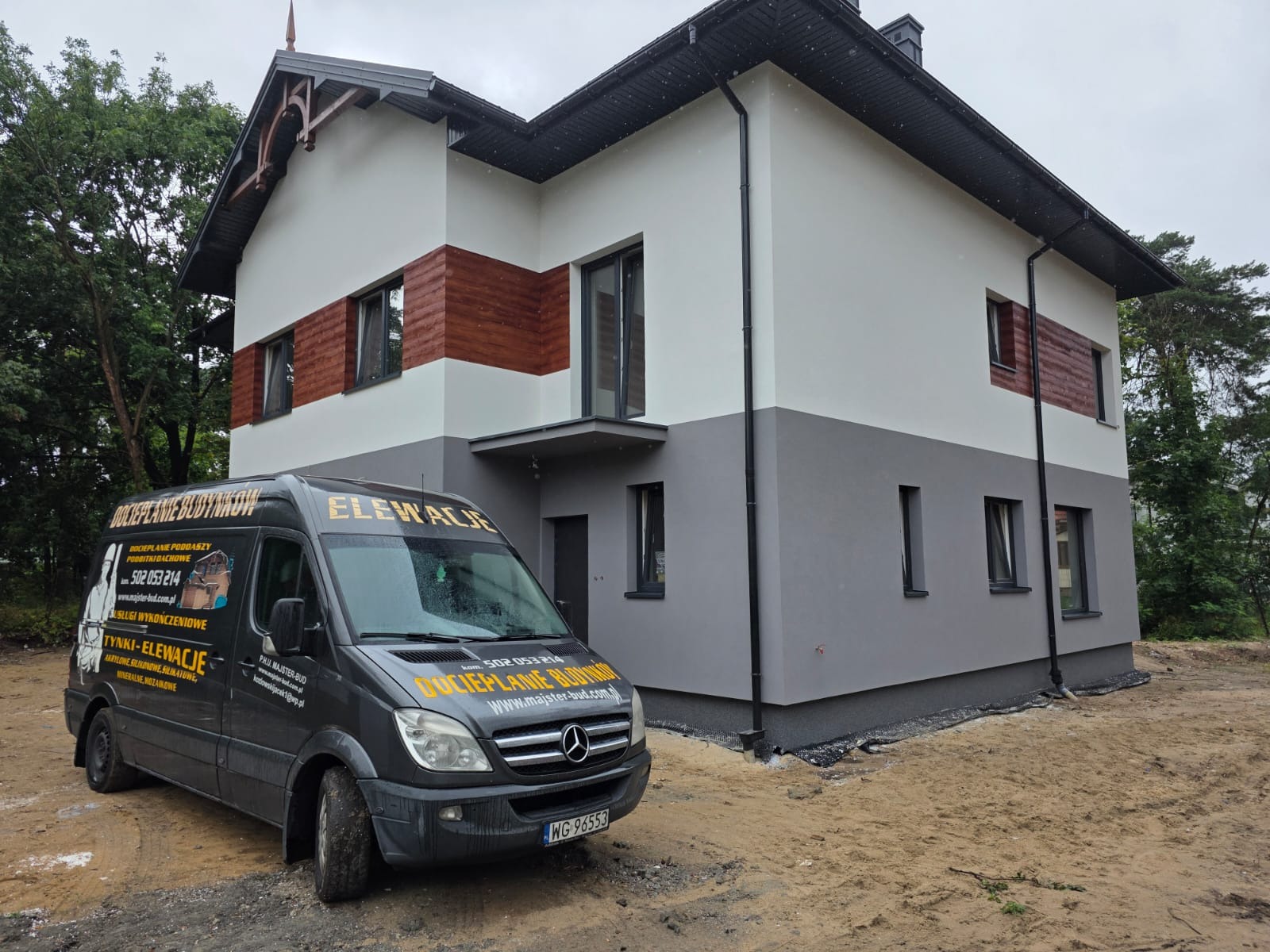 Dwukondygnacyjny dom z elewacją w odcieniach bieli i szarości, z elementami drewnianymi. Na pierwszym planie firmowy bus z reklamą usług elewacyjnych.