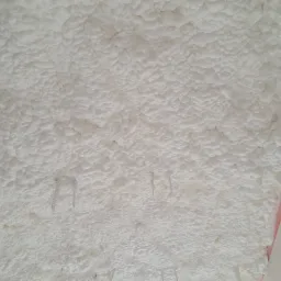 Pianka izolacyjna o strukturze popcornu, przytwierdzona do poddasza za pomocą metalowych zszywek; widoczne fragmenty konstrukcji dachu.