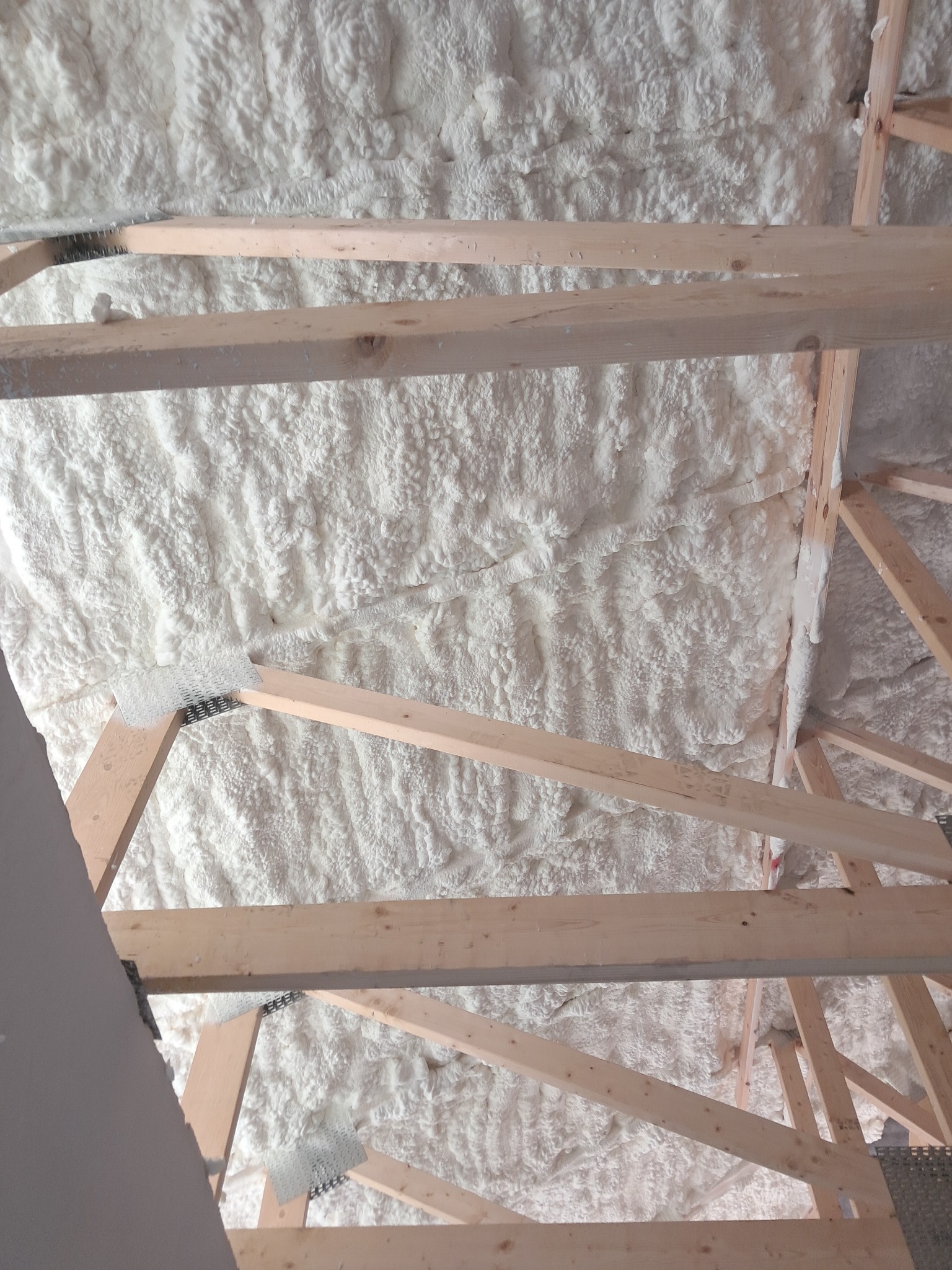 Sufit poddasza z drewnianą konstrukcją i zaaplikowaną warstwą izolacji pianką poliuretanową, widok od dołu.