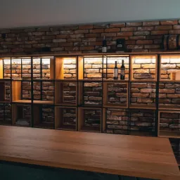 Loftowa aranżacja wnętrza z ceglaną ścianą, drewnianym regałem z podświetleniem i stołem z litego drewna.