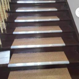 Ciemnobrązowe drewniane schody z antypoślizgowymi nakładkami z wykładziny i aluminiowymi listwami zabezpieczającymi krawędzie.