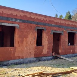 R Klawe Home firma budowlana Robert Klawe - Surowy stan domu z czerwonej cegły, widoczne otwory okienne i drzwiowe, betonowe nadproża. W tle drzewa i częściowo widoczny samochód dostawczy.